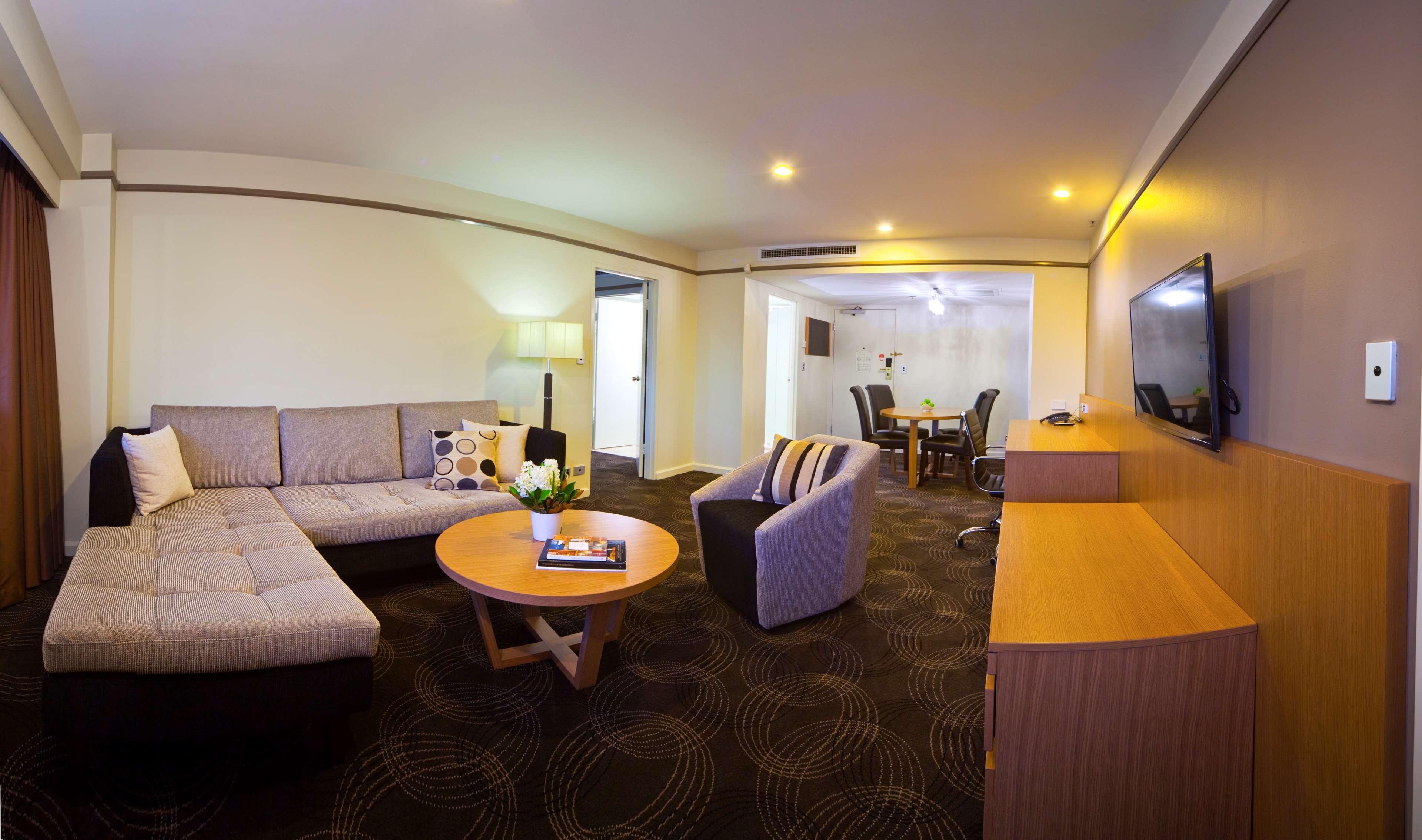 Stamford Plaza Adelaide Hotel ภายนอก รูปภาพ The photo shows a spacious living area with modern decor. On the left, there is a light gray sectional sofa, accompanied by a round wooden coffee table in front of it. A couple of decorative pillows add a touch of color to the sofa. To the right, the