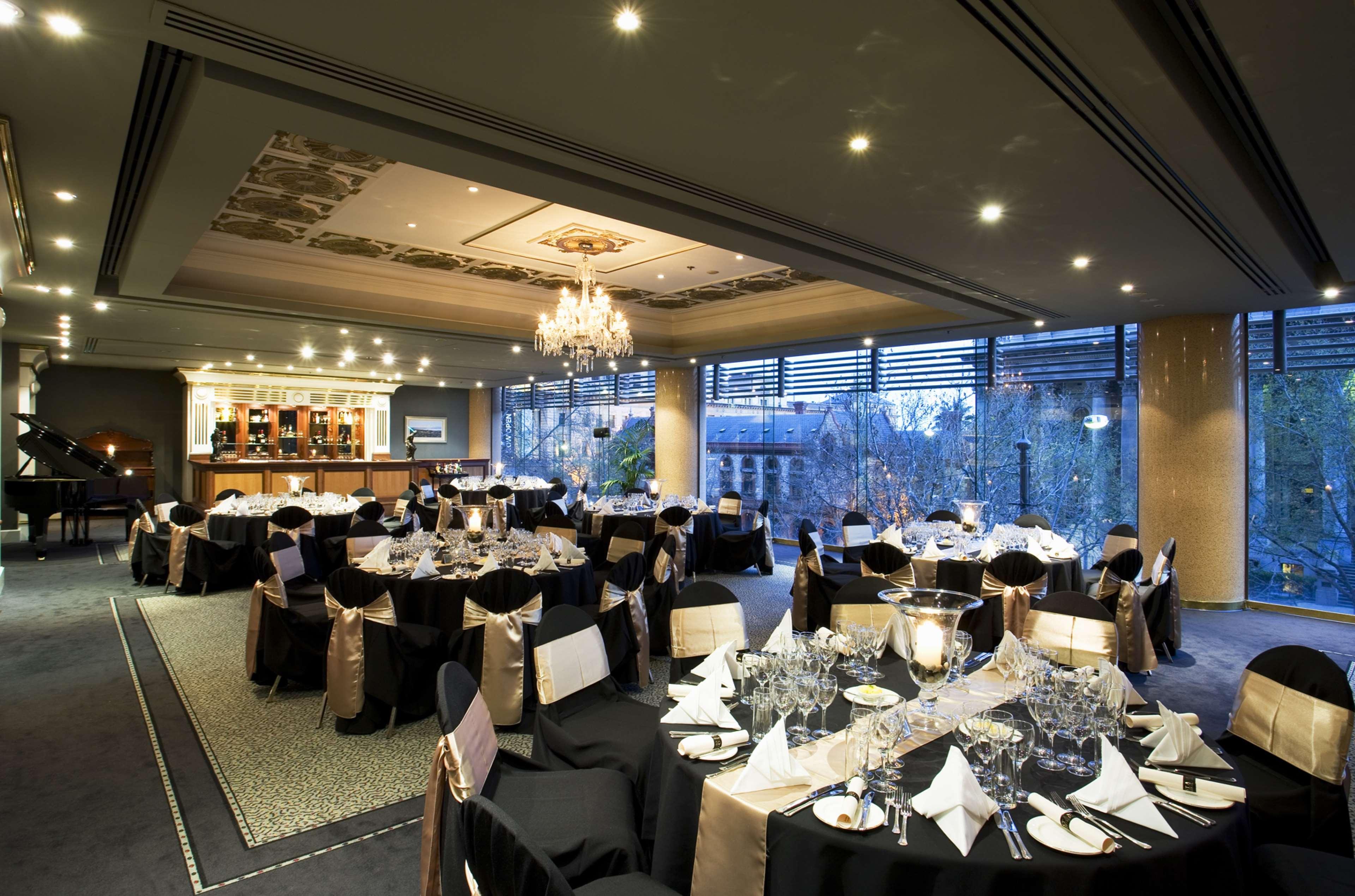Stamford Plaza Adelaide Hotel ภายนอก รูปภาพ The photo shows an elegant banquet hall or restaurant setting. There are several round tables covered with black tablecloths and adorned with gold accents. Each table is set with fine dining utensils, glassware, and neatly folded napkins. In the back