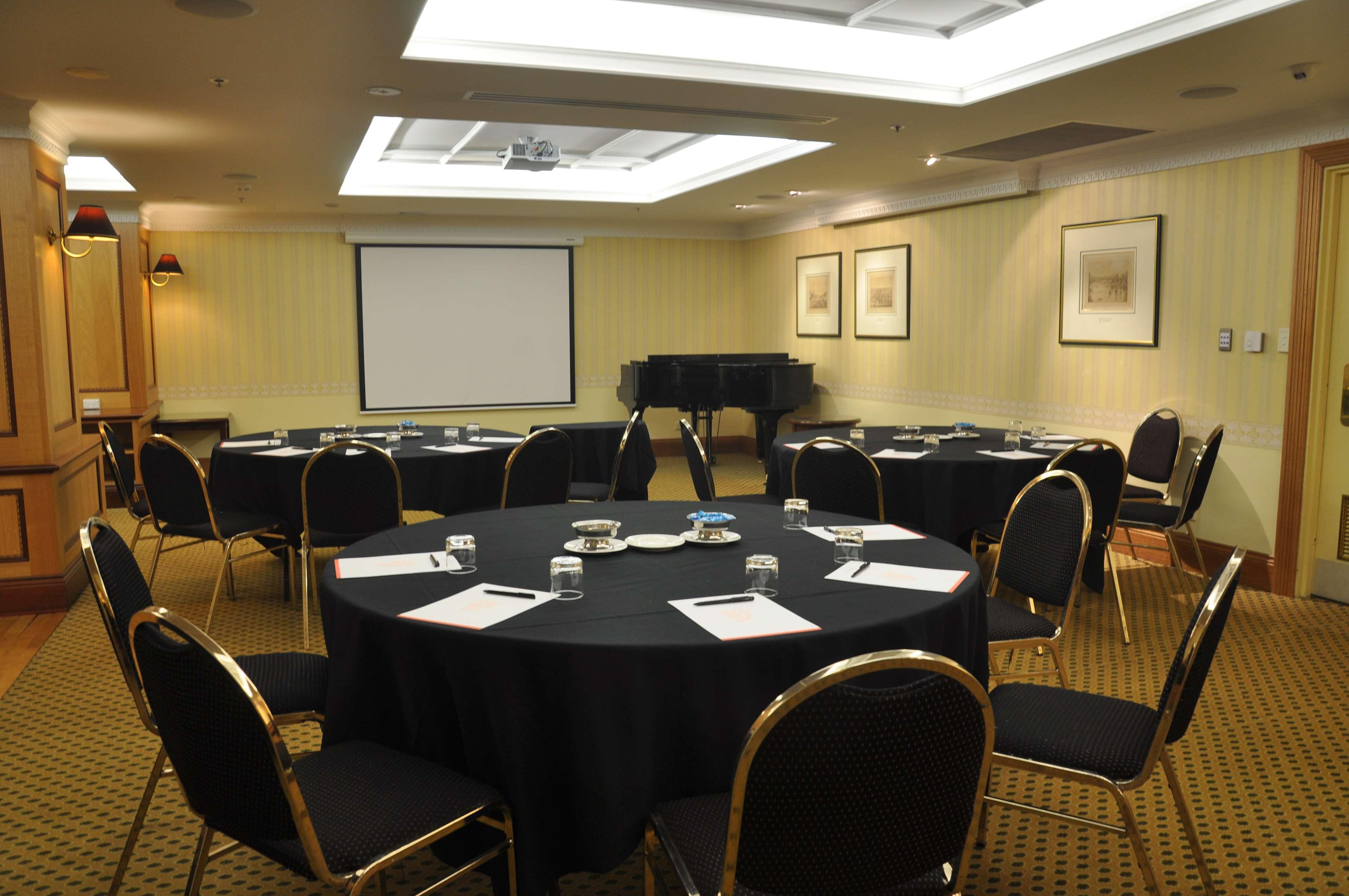 Stamford Plaza Adelaide Hotel ภายนอก รูปภาพ The photo shows a conference room set up for a meeting or presentation. There are several round tables covered with black tablecloths, each surrounded by black upholstered chairs. On the tables, there are notepads and glasses of water, indicating tha